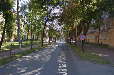 Współczesne zdjęcie. Przedstawia aleję drzew i budynki w mieście. Jest to ulica Jana III Sobieskiego w Częstochowie. 