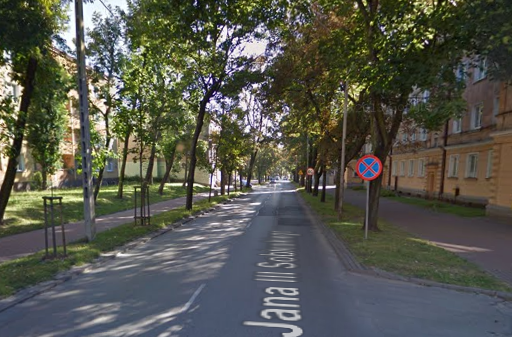 Współczesne zdjęcie. Przedstawia aleję drzew i budynki w mieście. Jest to ulica Jana III Sobieskiego w Częstochowie. 