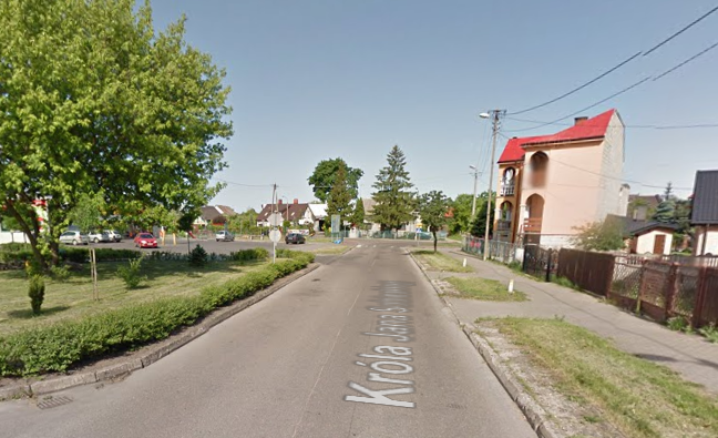 Współczesne zdjęcie. Przedstawia widok ulicy w mieście. Po prawej stronie pojedyncze budynki, po lewej drzewa i trawnik. Jest to Ulica Króla Jana Sobieskiego w Ostrołęce. 