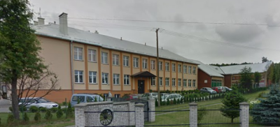 Współczesne zdjęcie. Przedstawia widok na budynek z wejściem, przed nim ogrodzenie. Jest to Zespół Szkół im. Króla Jana III Sobieskiego w Dłużcu. 