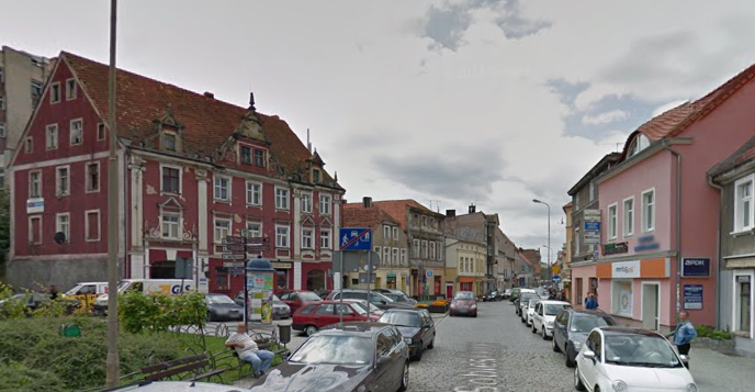 Współczesne zdjęcie. Przedstawia widok ulicy w mieście. Widzimy kolorowe kamienice i deptak oraz samochody zaparkowane przy ulicy. Jest to Ulica Jana Sobieskiego w Zielonej Górze. 