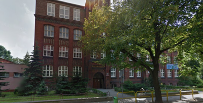 Współczesne zdjęcie. Przedstawia widok na zabytkowy budynek z czerwonej cegły. Jest to Publiczne Gimnazjum nr 1 im. Jana III Sobieskiego w Tarnowskich Górach. 