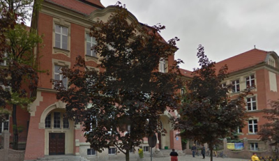 Współczesne zdjęcie. Przedstawia widok na zabytkowy budynek, przesłonięty drzewami. Jest to Szkoła Podstawowa nr 9 im. Króla Jana III Sobieskiego w Gliwicach. 