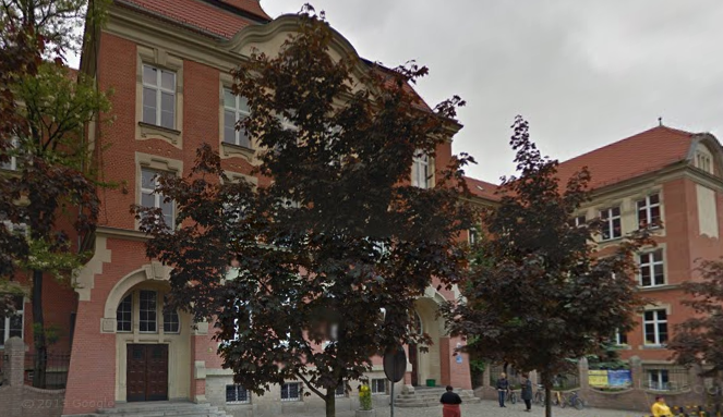 Współczesne zdjęcie. Przedstawia widok na zabytkowy budynek, przesłonięty drzewami. Jest to Szkoła Podstawowa nr 9 im. Króla Jana III Sobieskiego w Gliwicach. 