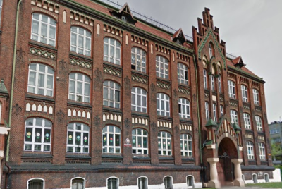 Współczesne zdjęcie. Przedstawia widok na reprezentacyjną fasadę budynku z czerwonej cegły. Jest to Szkoła Podstawowa nr 4 im. Jana III Sobieskiego w Rzeszowie. 