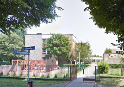 Współczesne zdjęcie. Przedstawia widok na budynek, przed którym stoi ogrodzenie. Jest to Szkoła Podstawowa nr 15 z Oddziałami Sportowymi im. Jana III Sobieskiego w Raciborzu. 