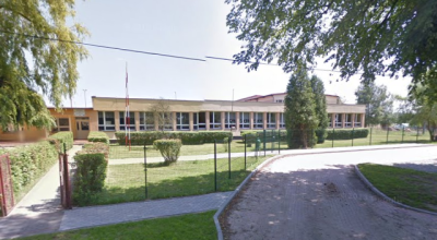 Współczesne zdjęcie. Przedstawia widok na niski, długi budynek z wejściem, przed nim ogrodzenie i droga. Jest to Zespół Szkół im. Jana III Sobieskiego w Brzeźnie Szlacheckim.