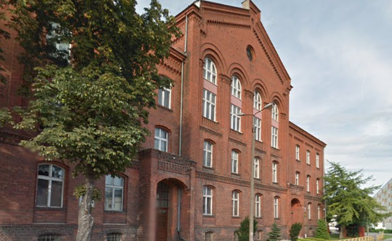 Współczesne zdjęcie. Przedstawia widok na pomarańczową, ceglaną fasadę starej budowli. Jest to Gimnazjum nr 1 im. Jana III Sobieskiego w Malborku. 