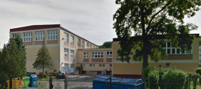 Współczesne zdjęcie. Przedstawia widok na budynek szkoły za ogrodzeniem. Jest to I Liceum Ogólnokształcące im. Króla Jana III Sobieskiego w Wejherowie. 