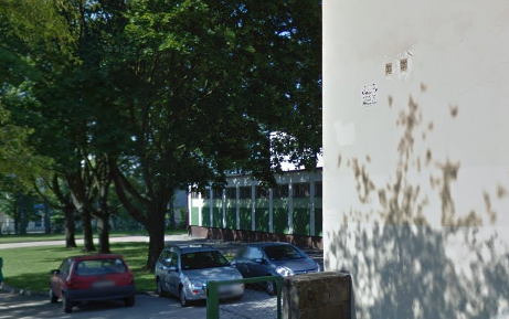 Współczesne zdjęcie. Przedstawia widok na budynek, przesłonięty drzewami. Z przodu parking i samochody. Jest to Publiczne Gimnazjum nr 3 im. Jana III Sobieskiego w Opolu. 