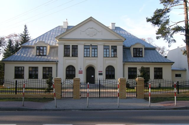 Współczesne zdjęcie. Przedstawia widok na fasadę zabytkowego budynku. Jest to Szkoła Podstawowa im. Króla Jana III Sobieskiego w Puszczy Mariańskiej. 