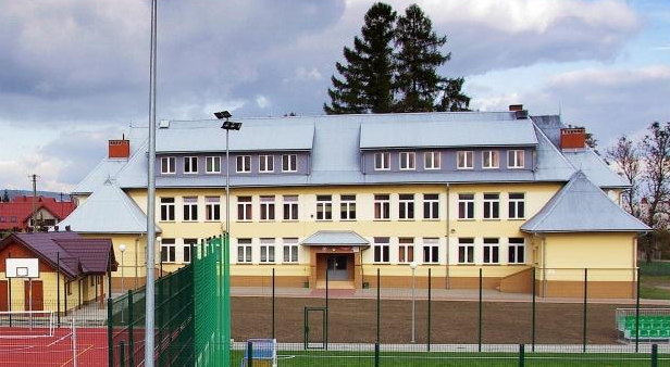 Współczesne zdjęcie. Przedstawia widok na żółty budynek z szarym dachem. Jest to Szkoła Podstawowa  im. Jana III Sobieskiego w Brzeznej. 