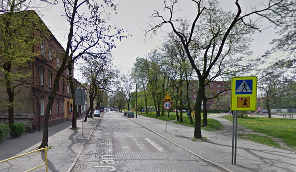 Współczesne zdjęcie. Przedstawia widok na ulicę wraz z zabudowaniami miejskimi. Jest to Ulica Jana III Sobieskiego w Zabrzu. 