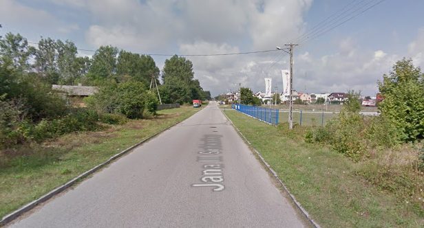 Współczesne zdjęcie. Przedstawia widok na miejską ulicę wraz z zabudowaniami. Jest to Ulica Jana III Sobieskiego we Włoszczowej. 