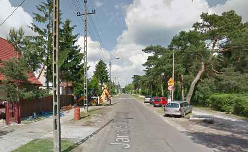 Współczesne zdjęcie. Przedstawia widok na ulicę w małym mieście. Po lewej stronie domki, po prawej stronie parking z samochodami. Jest to Ulica Jana Sobieskiego w Józefowie. 