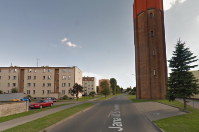 Współczesne zdjęcie. Przedstawia widok na ulicę i zabudowania miejskie. Są to niskie bloki, z prawej strony wysoka wieża z cegły. Jest to ulica Jana III Sobieskiego w Człuchowie.