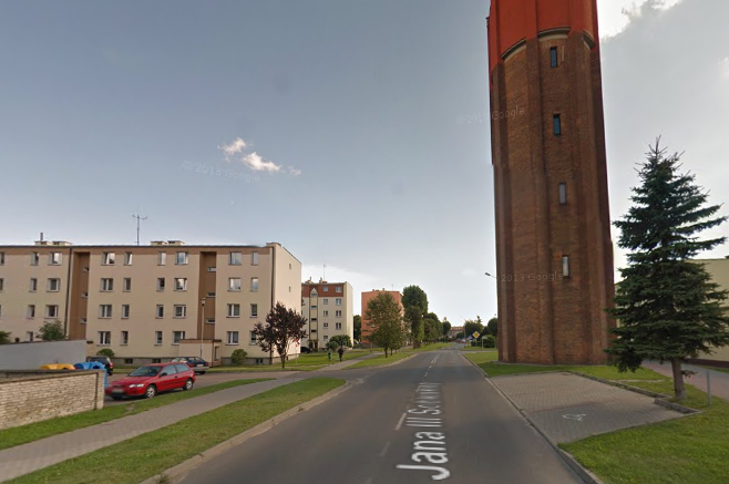 Współczesne zdjęcie. Przedstawia widok na ulicę i zabudowania miejskie. Są to niskie bloki, z prawej strony wysoka wieża z cegły. Jest to ulica Jana III Sobieskiego w Człuchowie.