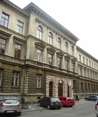 Kolorowa, współczesna fotografia. Przedstawia ulicę i długi budynek. Jest to m.in. Liceum im. Jana III Sobieskiego w Krakowie. Szkoła do dzisiaj mieści się przy ulicy Sobieskiego. Na ulicy stoją kolorowe samochody. 