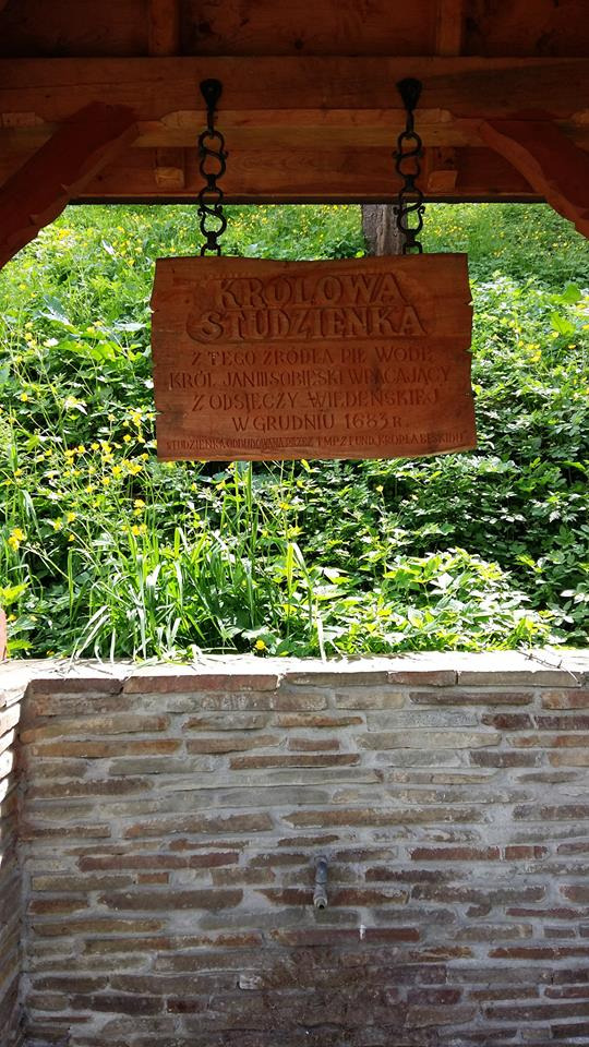 Współczesne zdjęcie. Przedstawia tablicę przymocowaną łańcuchami do drewnianej belki konstrukcyjnej nad studnią. Na tablicy napis: Królowa Studzienka. Studnia znajduje się w pobliżu ulicy Sobieskiego w Piwnicznej-Zdroju. Wedle lokalnej tradycji wodę z tryskającego tu źródła pił król Jan III podczas powrotu spod Wiednia. 