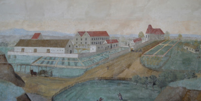 Obraz przedstawia widok na zabudowania, białe domy z pomarańczowymi dachami. Wokół zielone pola uprawne i grządki.