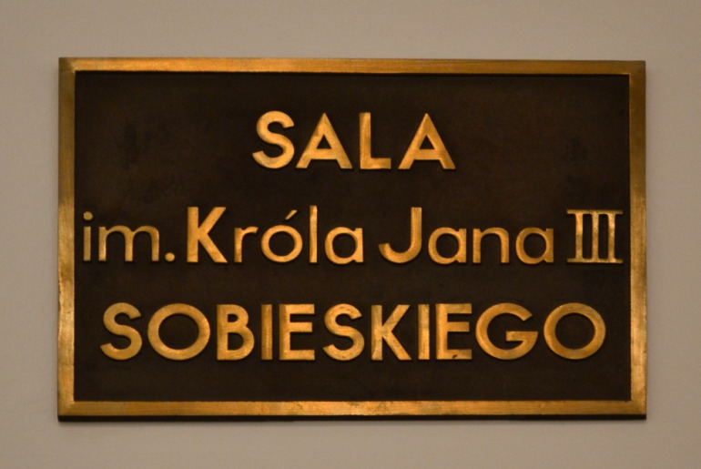 Zdjęcie przedstawia płytę z napisem Sala im. Króla Jana III Sobieskiego. Jest to sala konferencyjna w Stacji Naukowej Polskiej Akademii Nauk. 