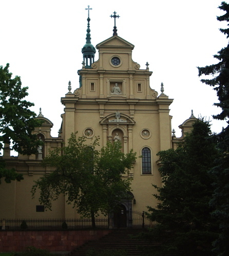 Kolorowe zdjęcie współczesne. Przedstawia widok na fasadę kościoła. Jest to barokowa fasada katedry w Kielcach z rzeźbami w niszach. 