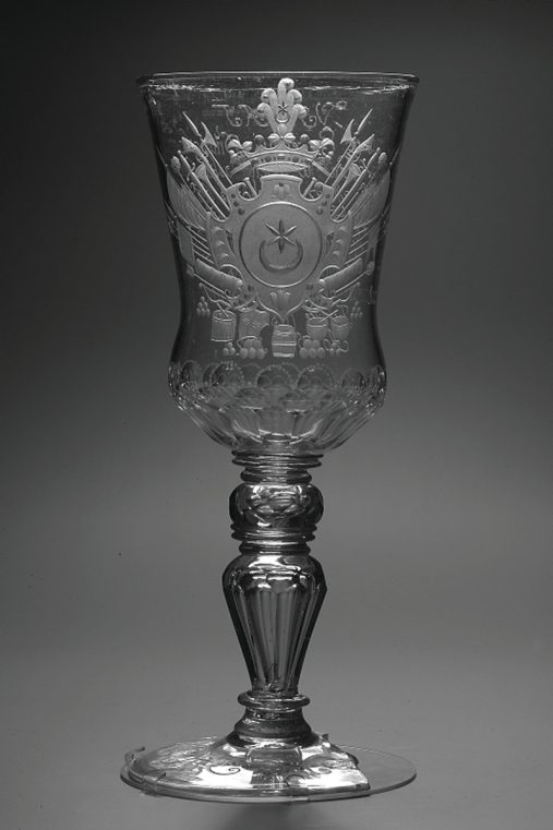 Wysoki kielich ze szkła z okrągłą podstawą i nóżką. Kielich z herbem „Leliwa” i napisem dedykacyjnym dla Adama Mikołaja Sieniawskiego, hetmana wielkiego koronnego, kasztelana krakowskiego. 