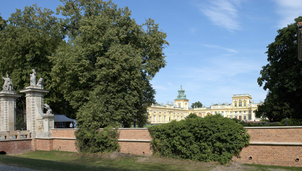 Mur porośnięty bluszczem, obok brama główna, w tle pałac wilanowski.