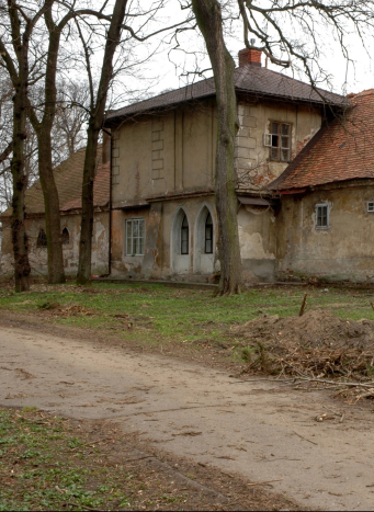 Niszczejący szary budynek z obdrapanym tynkiem.