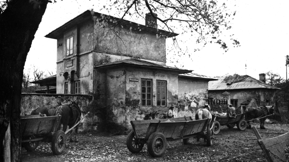 Domek Lanciego na czarnobiałej fotografii archiwalnej. Na pierwszym planie wozy z końmi.